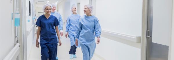 A smiling group of nurses in surgical attire walk down a hospital hallway.